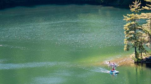 guests paddling and kayaking near the shoreline of stratton resort’s scenic swimming hole, surrounded by forest and clear mountain water